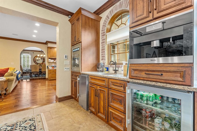 kitchen with sink, light stone counters, ornamental molding, wine cooler, and light wood-type flooring