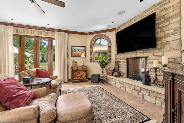 living room featuring french doors, ceiling fan, light tile floors, ornamental molding, and a stone fireplace