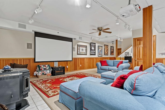 tiled home theater room featuring a wood stove, ceiling fan, and rail lighting