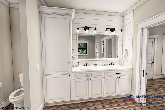 bathroom featuring dual sinks, toilet, hardwood / wood-style flooring, vanity with extensive cabinet space, and crown molding