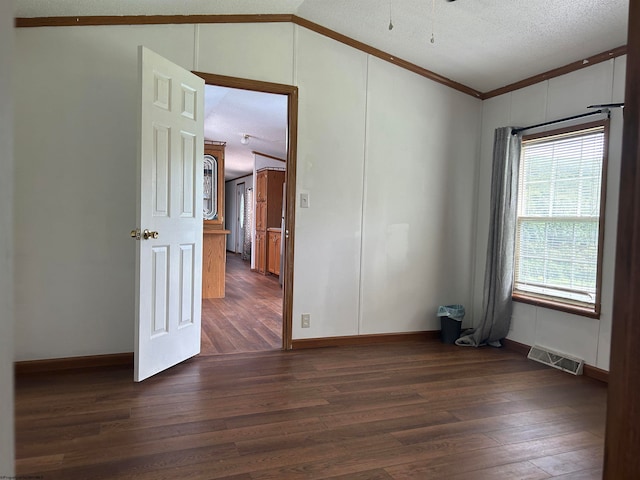 empty room featuring vaulted ceiling, a textured ceiling, ornamental molding, and dark wood-type flooring