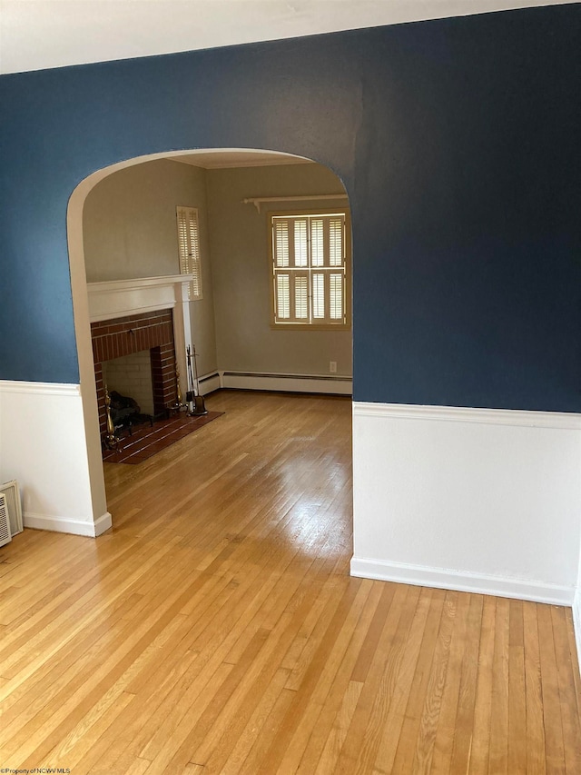 unfurnished living room with light wood-type flooring, a fireplace, and a baseboard heating unit