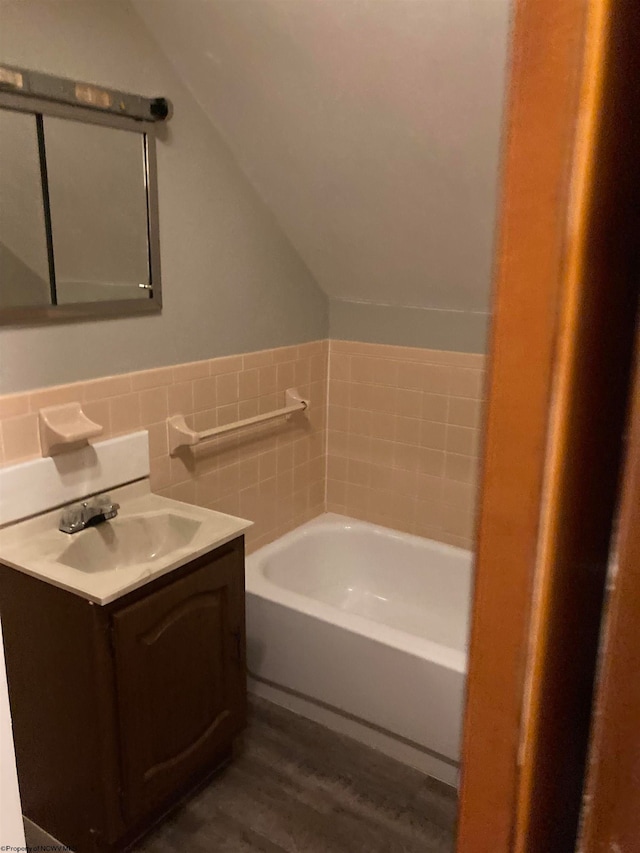 bathroom with oversized vanity, hardwood / wood-style floors, backsplash, lofted ceiling, and a washtub