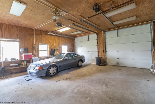 garage featuring wood walls, ceiling fan, and a garage door opener