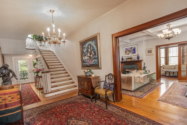 entryway featuring beamed ceiling, a fireplace, a chandelier, ornamental molding, and hardwood / wood-style flooring