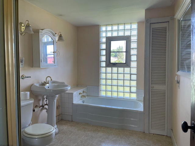 bathroom with toilet, a washtub, a wealth of natural light, and tile patterned flooring