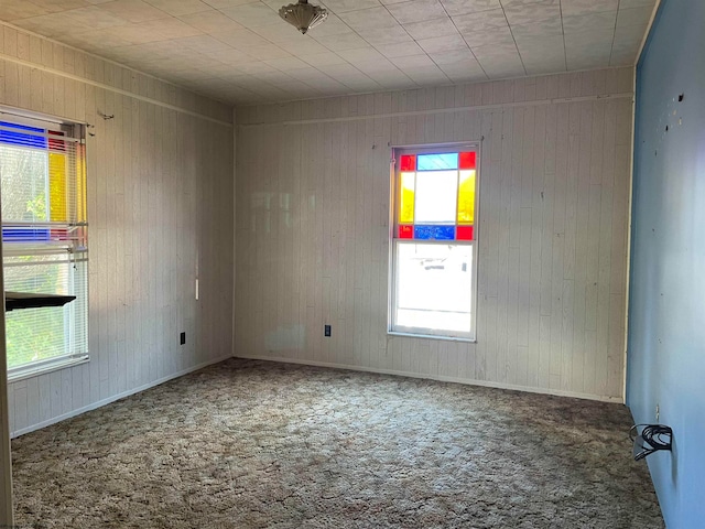 carpeted spare room featuring wooden walls and baseboards