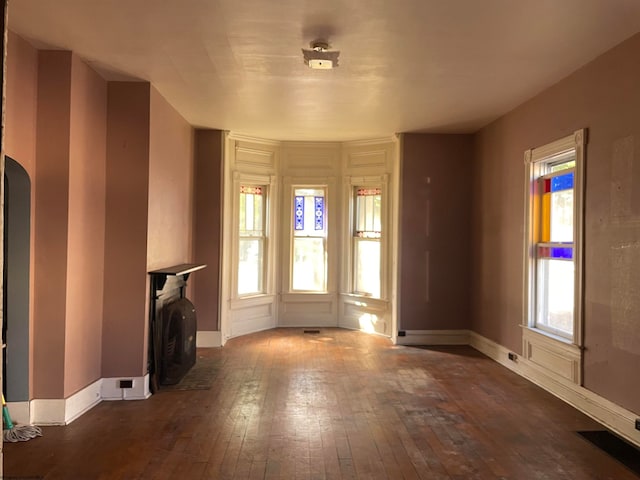 unfurnished living room with arched walkways, dark wood finished floors, visible vents, and baseboards