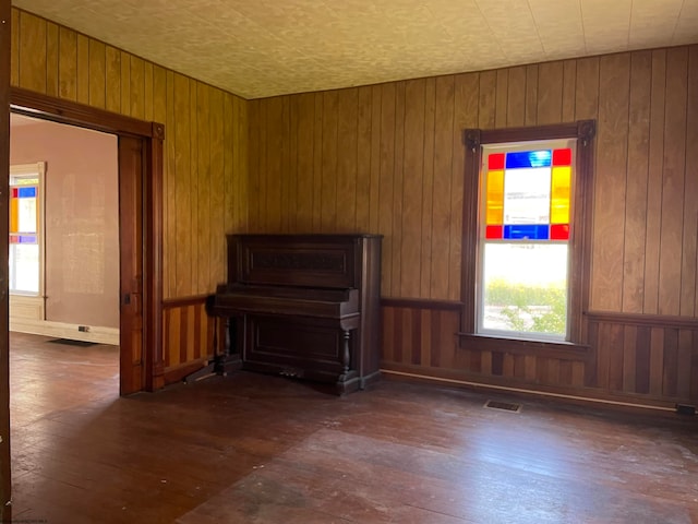 unfurnished living room featuring dark wood-style floors, visible vents, and wood walls