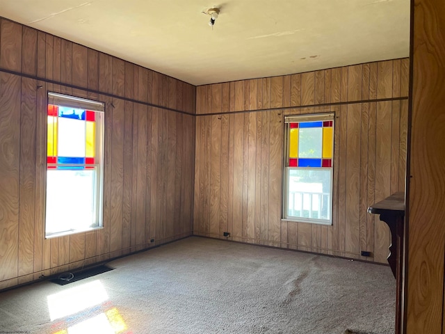 spare room featuring light carpet, visible vents, plenty of natural light, and wood walls