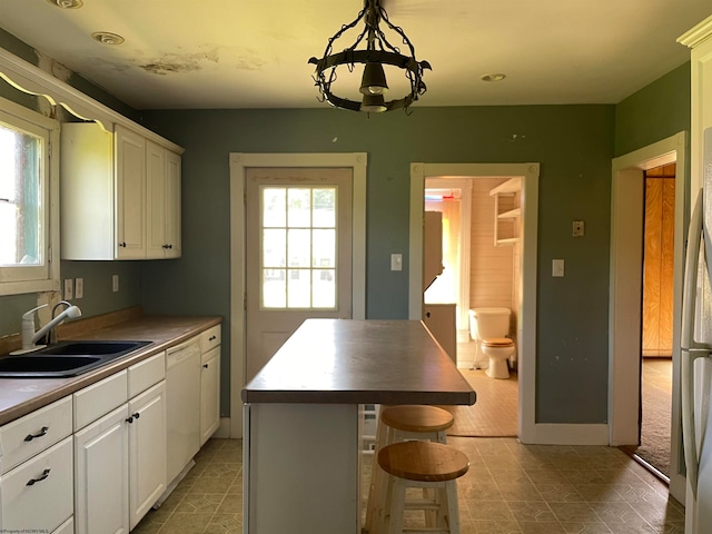 kitchen with white cabinets, a center island, hanging light fixtures, white dishwasher, and a sink