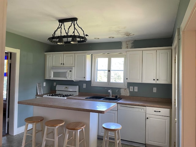 kitchen with white appliances, a breakfast bar, a sink, white cabinets, and pendant lighting