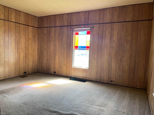 empty room featuring wood walls, carpet flooring, and visible vents