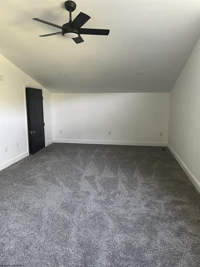 interior space with baseboards, dark carpet, vaulted ceiling, and a ceiling fan