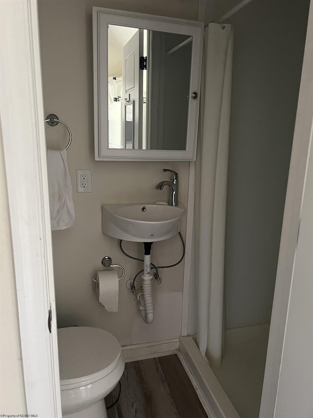 bathroom featuring baseboards, toilet, wood finished floors, curtained shower, and a sink