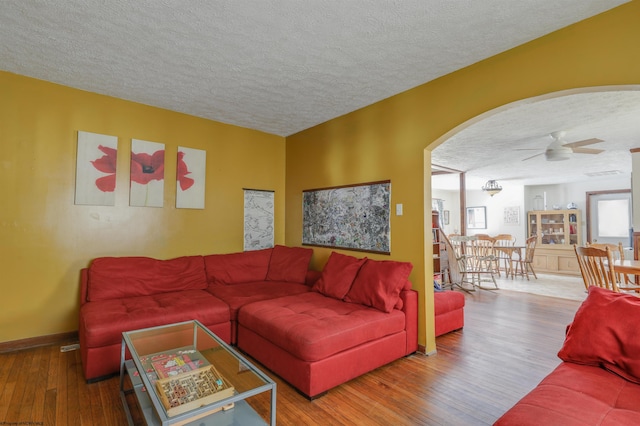 living room with a textured ceiling, ceiling fan, and wood-type flooring