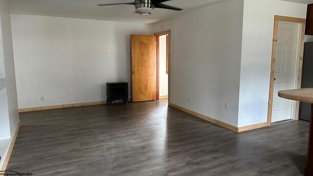 empty room featuring ceiling fan, a wood stove, and dark hardwood / wood-style floors