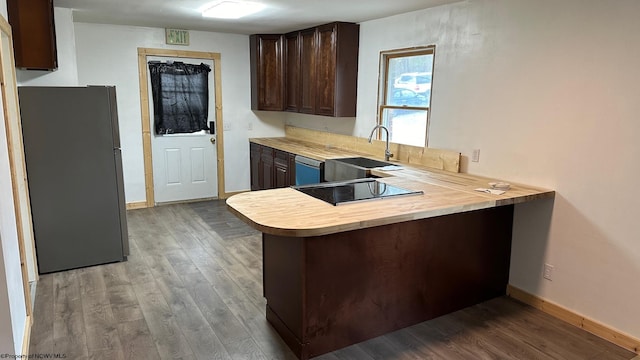 kitchen with sink, kitchen peninsula, stainless steel appliances, dark brown cabinetry, and light hardwood / wood-style flooring