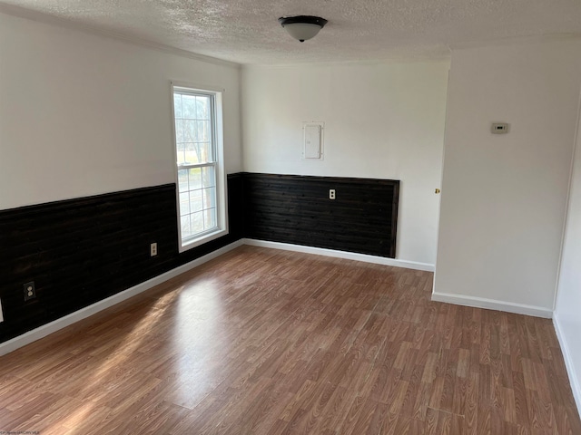 empty room with wood-type flooring, a textured ceiling, and electric panel