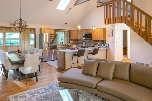 living room featuring sink, a skylight, high vaulted ceiling, a chandelier, and light wood-type flooring