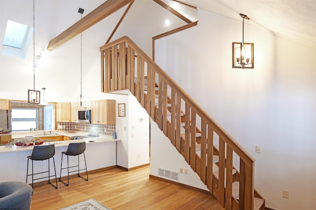 staircase with hardwood / wood-style flooring, a skylight, high vaulted ceiling, and beam ceiling