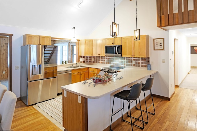 kitchen featuring stainless steel appliances, decorative light fixtures, light hardwood / wood-style floors, and kitchen peninsula