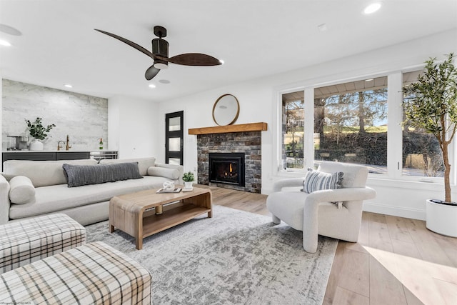 living room with a brick fireplace, light hardwood / wood-style flooring, sink, and ceiling fan