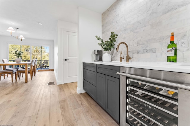 bar with decorative light fixtures, tasteful backsplash, sink, beverage cooler, and light hardwood / wood-style flooring