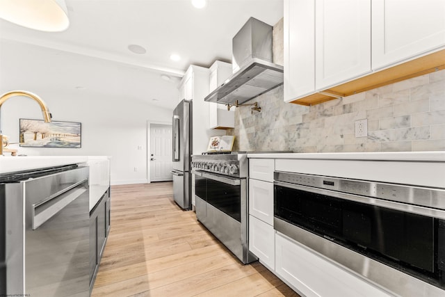 kitchen with light hardwood / wood-style flooring, appliances with stainless steel finishes, range hood, tasteful backsplash, and white cabinets