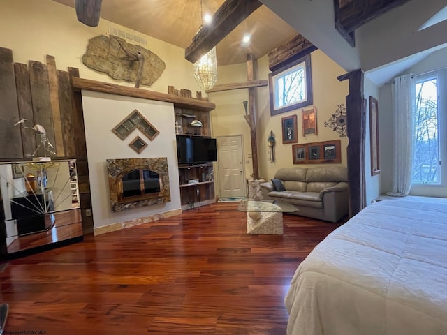 bedroom featuring a fireplace, multiple windows, a towering ceiling, and dark hardwood / wood-style flooring