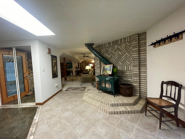 sitting room with ceiling fan, a wood stove, brick wall, and light tile floors