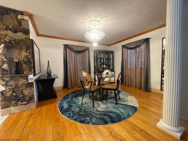 dining space with crown molding, light hardwood / wood-style flooring, decorative columns, an inviting chandelier, and a textured ceiling