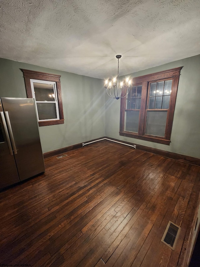 unfurnished dining area featuring a textured ceiling, dark hardwood / wood-style flooring, and a chandelier