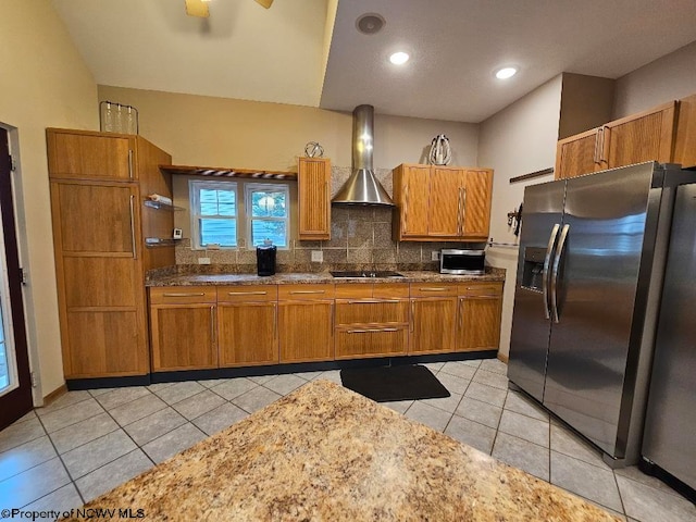 kitchen featuring dark stone counters, appliances with stainless steel finishes, tasteful backsplash, wall chimney range hood, and light tile flooring