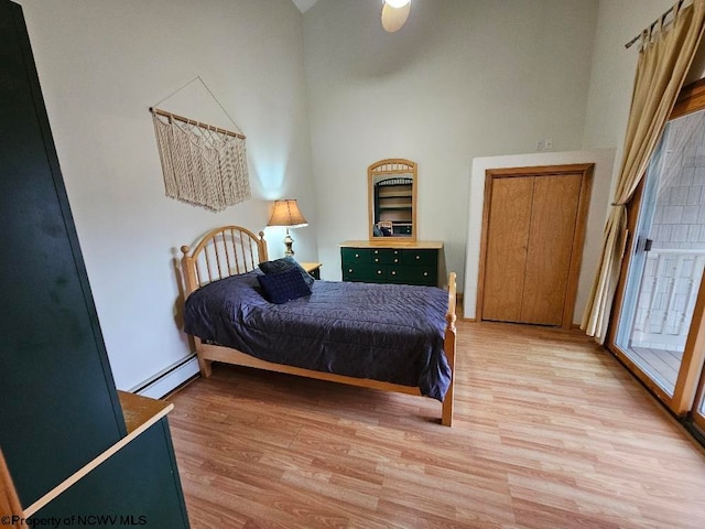 bedroom featuring a baseboard radiator, light hardwood / wood-style floors, and a towering ceiling