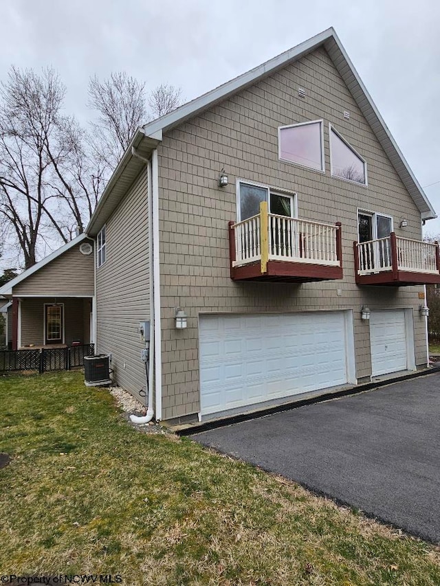 rear view of property featuring a balcony, central air condition unit, a lawn, and a garage