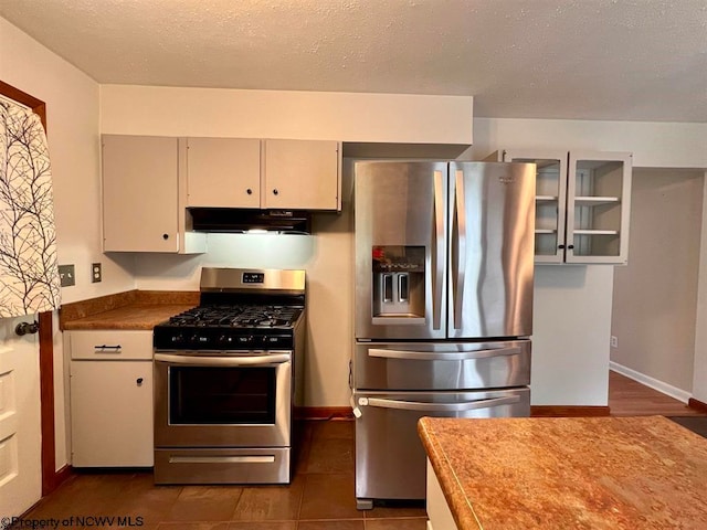 kitchen with dark tile floors, stainless steel appliances, white cabinetry, and range hood