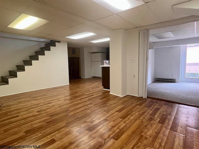 basement featuring a paneled ceiling, white refrigerator, hardwood / wood-style floors, and a baseboard heating unit