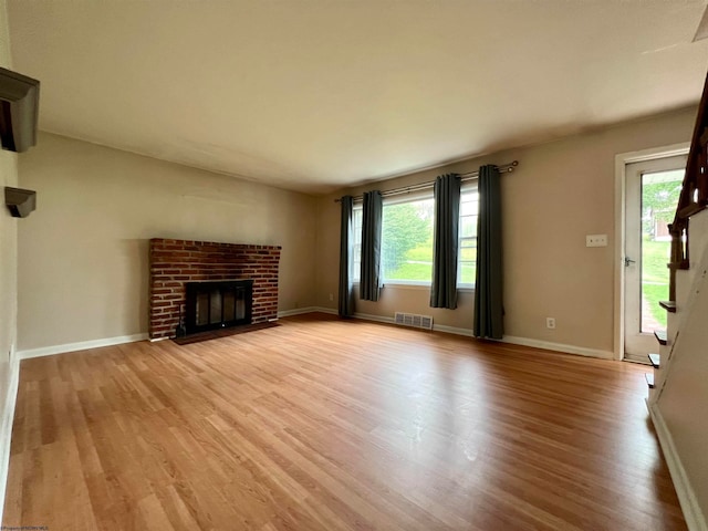 unfurnished living room with a brick fireplace, light hardwood / wood-style floors, and a healthy amount of sunlight