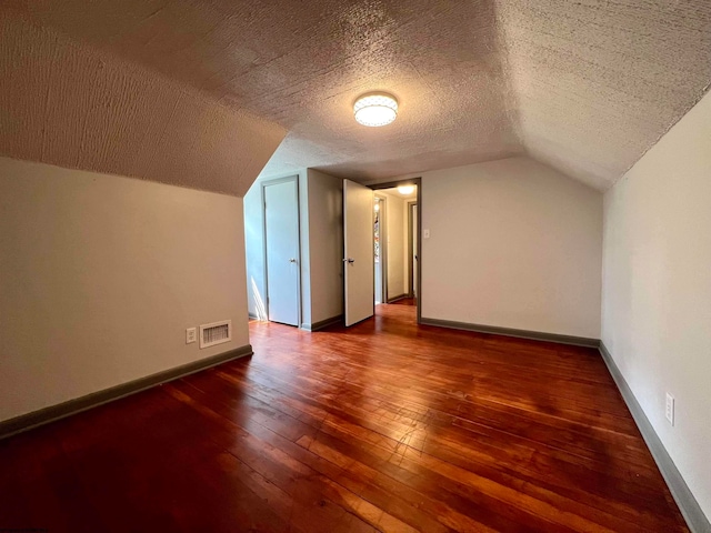 additional living space with lofted ceiling, a textured ceiling, and dark hardwood / wood-style floors