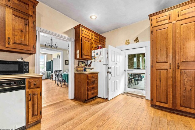 kitchen with light hardwood / wood-style flooring, white appliances, an inviting chandelier, and vaulted ceiling