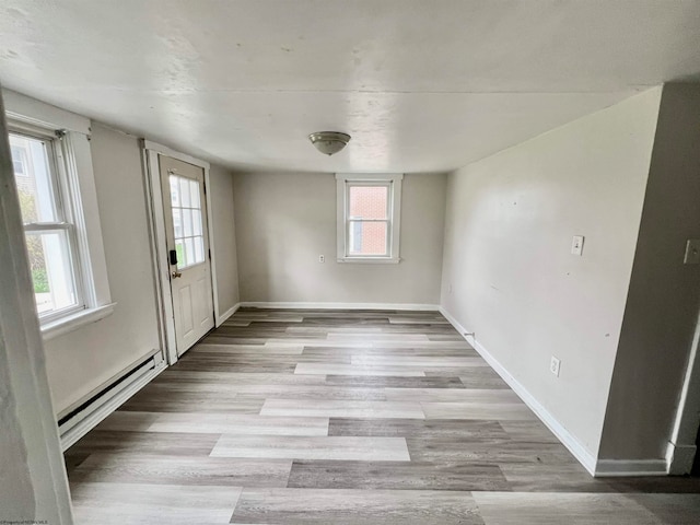 empty room with a healthy amount of sunlight, light hardwood / wood-style floors, and baseboard heating