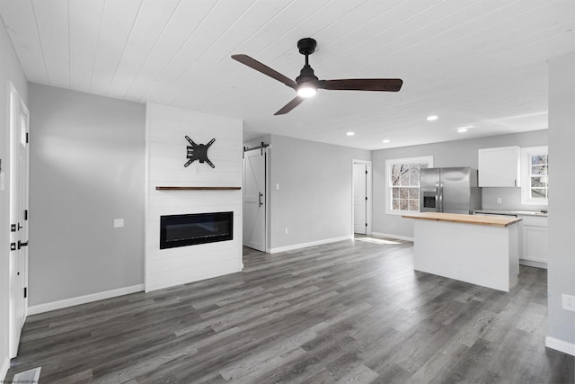 unfurnished living room with a barn door, a fireplace, ceiling fan, and dark hardwood / wood-style flooring