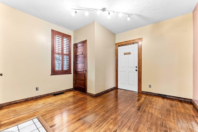 unfurnished room featuring hardwood / wood-style floors, a textured ceiling, and track lighting