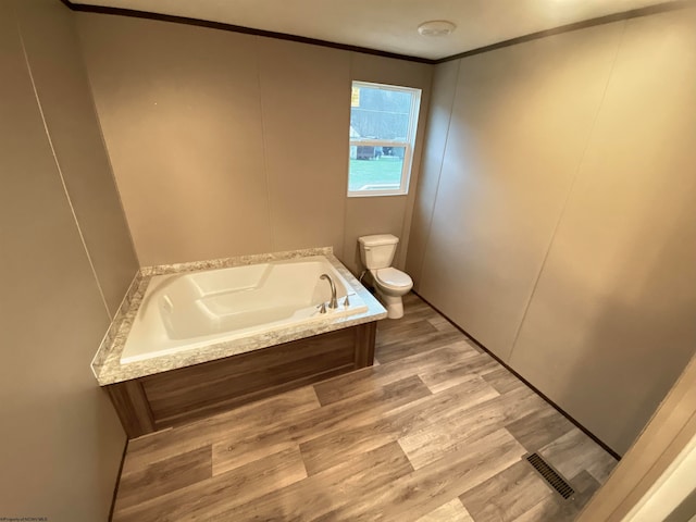 bathroom with a tub to relax in, toilet, and crown molding