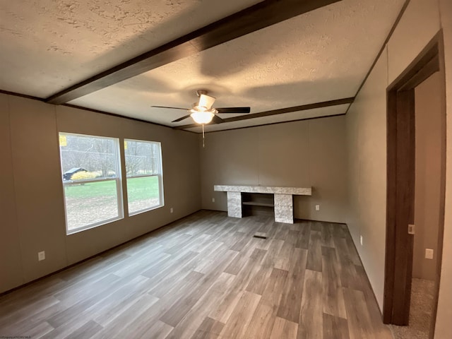 unfurnished bedroom with a textured ceiling, ceiling fan, beamed ceiling, and wood-type flooring