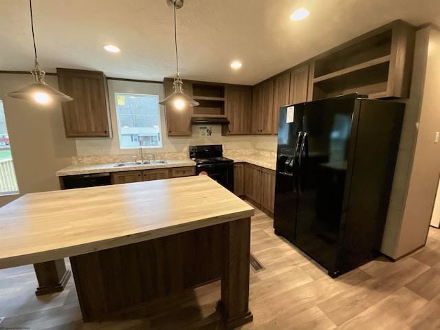 kitchen with light wood-type flooring, decorative light fixtures, black appliances, wooden counters, and sink