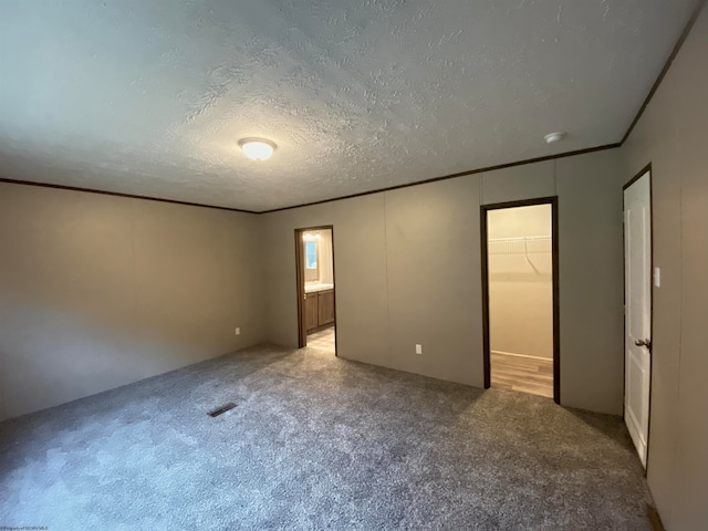 unfurnished bedroom with a walk in closet, carpet, a closet, and a textured ceiling