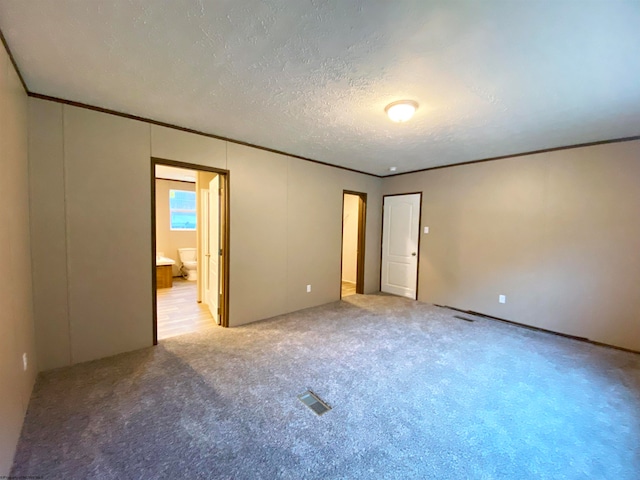 unfurnished bedroom featuring light carpet, a textured ceiling, ornamental molding, and ensuite bath