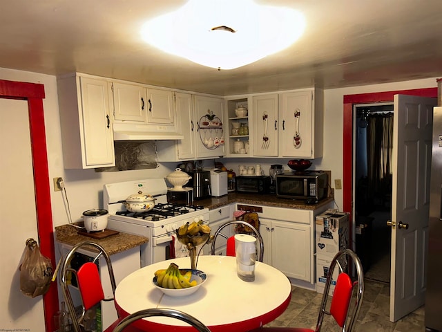 kitchen with dark stone counters, dark tile floors, white range with gas cooktop, and white cabinetry